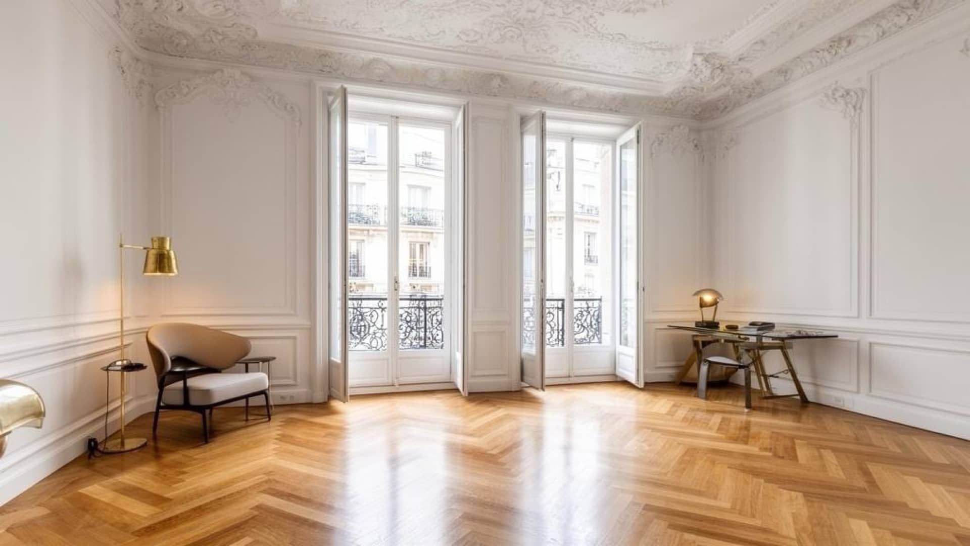 Salon ancien vide : plafond à décors de stuc, portes-fenêtres sur balcon en fonte, parquet en point de Hongrie