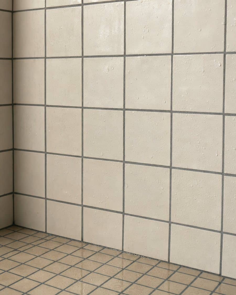 Mur de douche en petits carreaux blancs aux joints époxy gris réguliers, gouttes d’eau