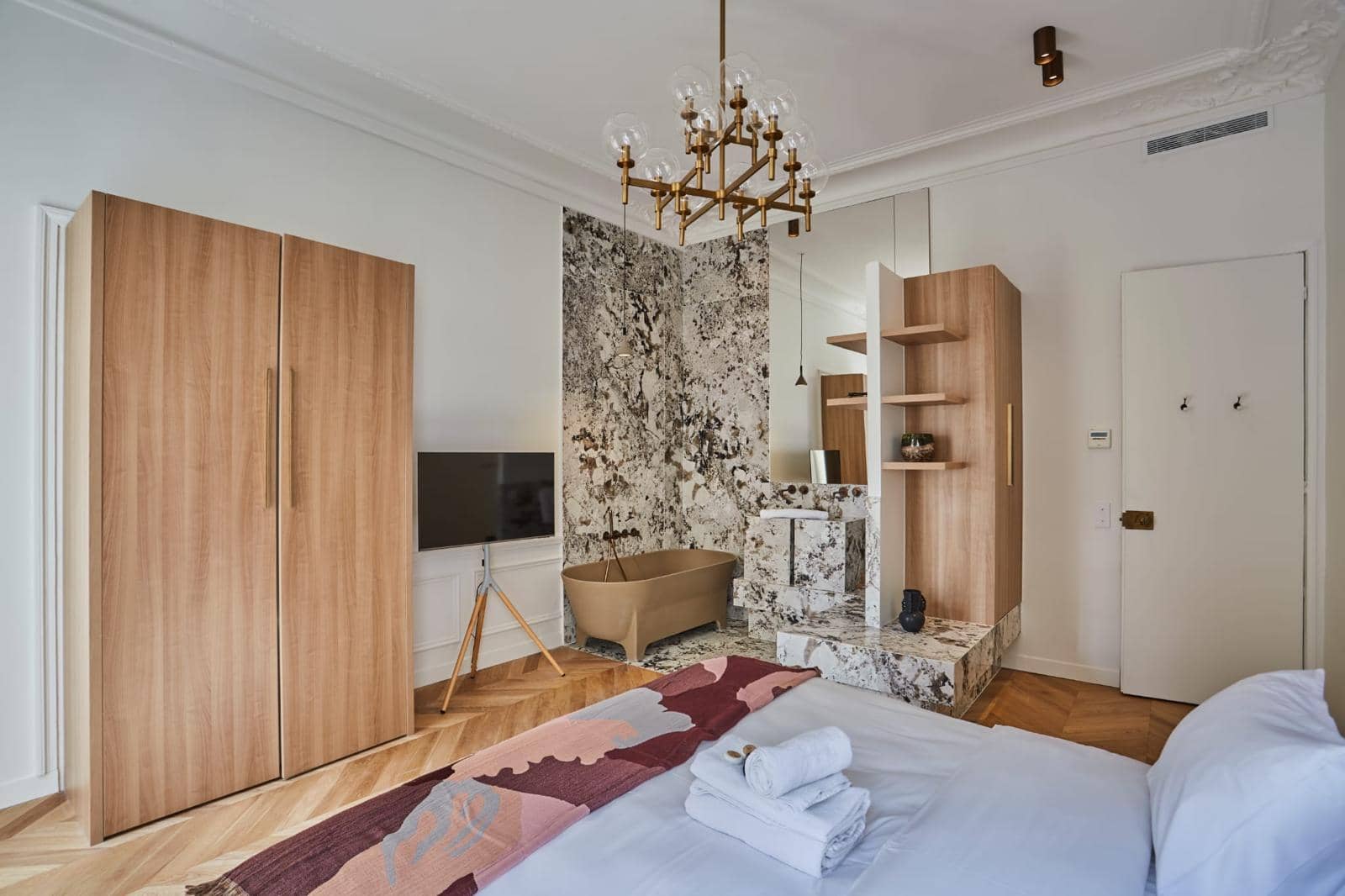 Suite parentale d'un appartement ancien : baignoire ouverte sur la chambre dans un écrin de granit, lustre et parquet