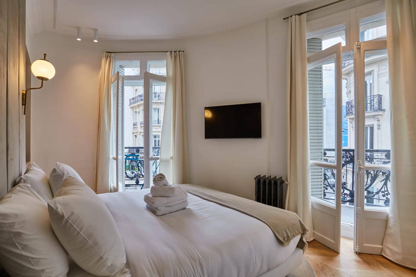 Chambre d'un appartement ancien rénové, portes-fenêtres ouvertes sur balcons en fonte et façades en pierre