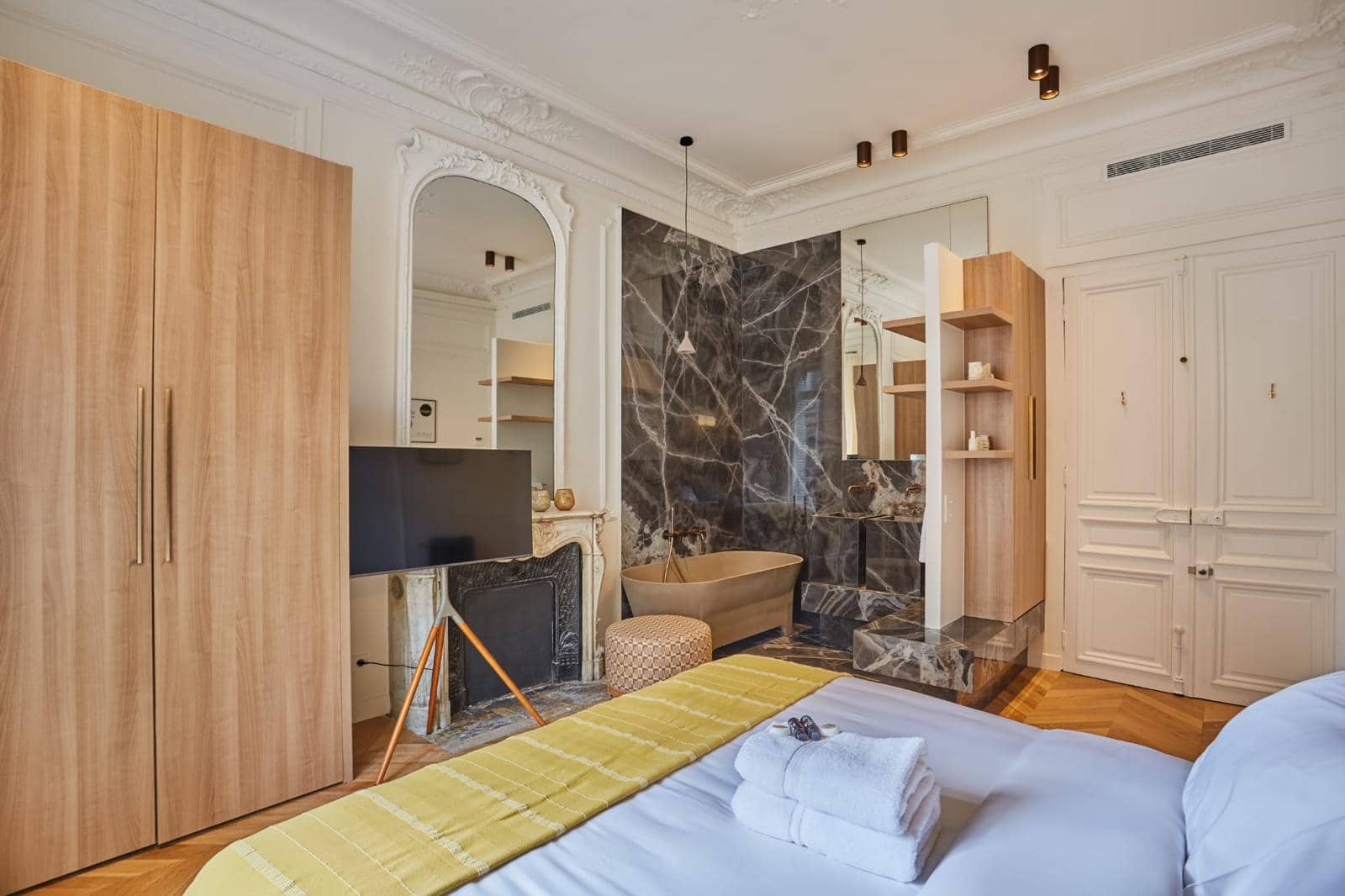 Chambre d'un appartement ancien avec salle de bains ouverte en marbre sombre, cheminée et parquet