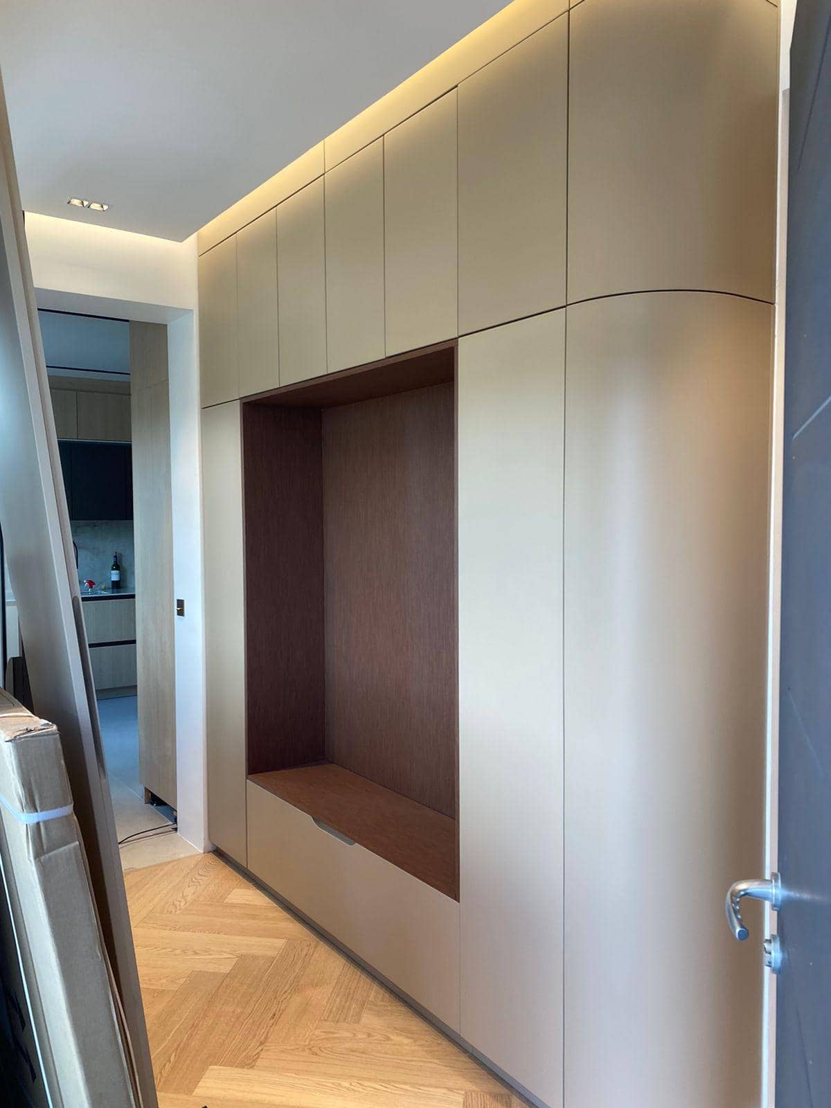 Entrée avec rangement intégré toute hauteur aux angles arrondis, niche banc habillée de bois et parquet à chevrons