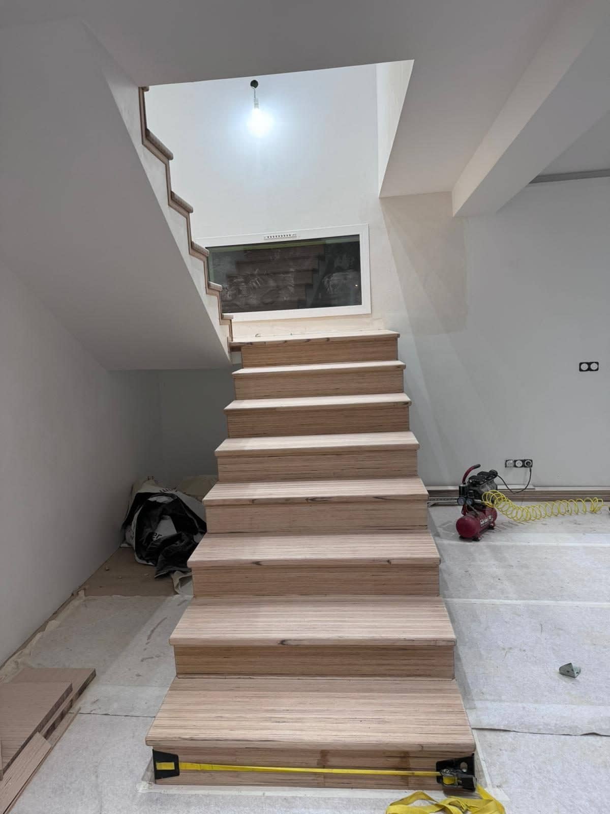 Escalier en bois en cours de pose, vu du niveau inférieur, montant vers une trémie ouverte dans le plancher