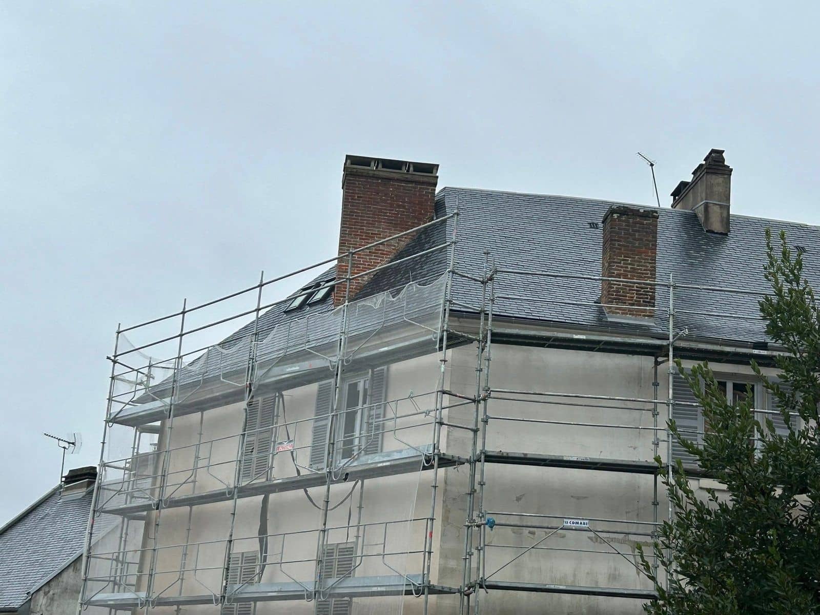 Maison ancienne à toit d'ardoise sous échafaudage pendant le ravalement de sa façade