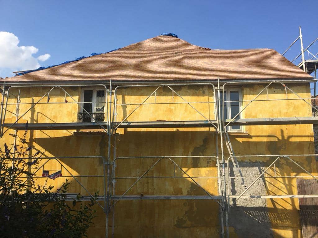 Maison ancienne sous échafaudage, toiture neuve en tuiles plates et façade enduite ocre en cours de reprise