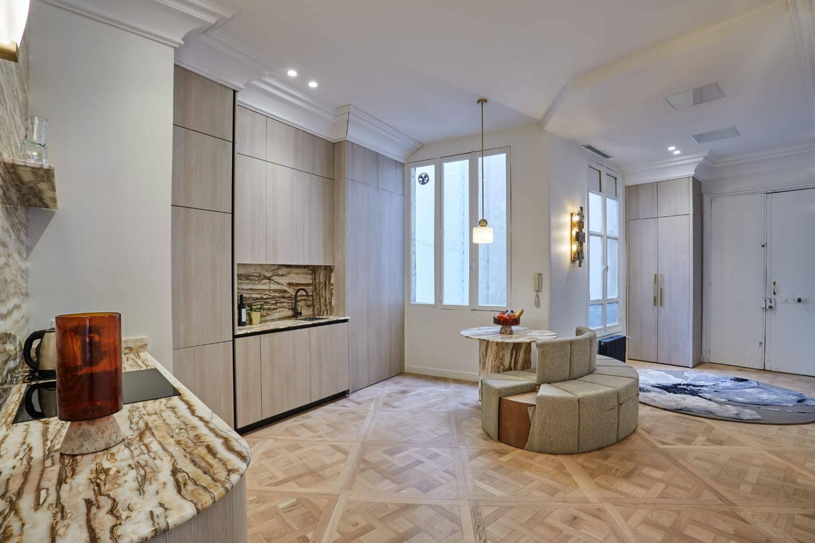 Pièce de vie d'un appartement ancien rénové : cuisine ouverte, coin salon et parquet en panneaux de Versailles