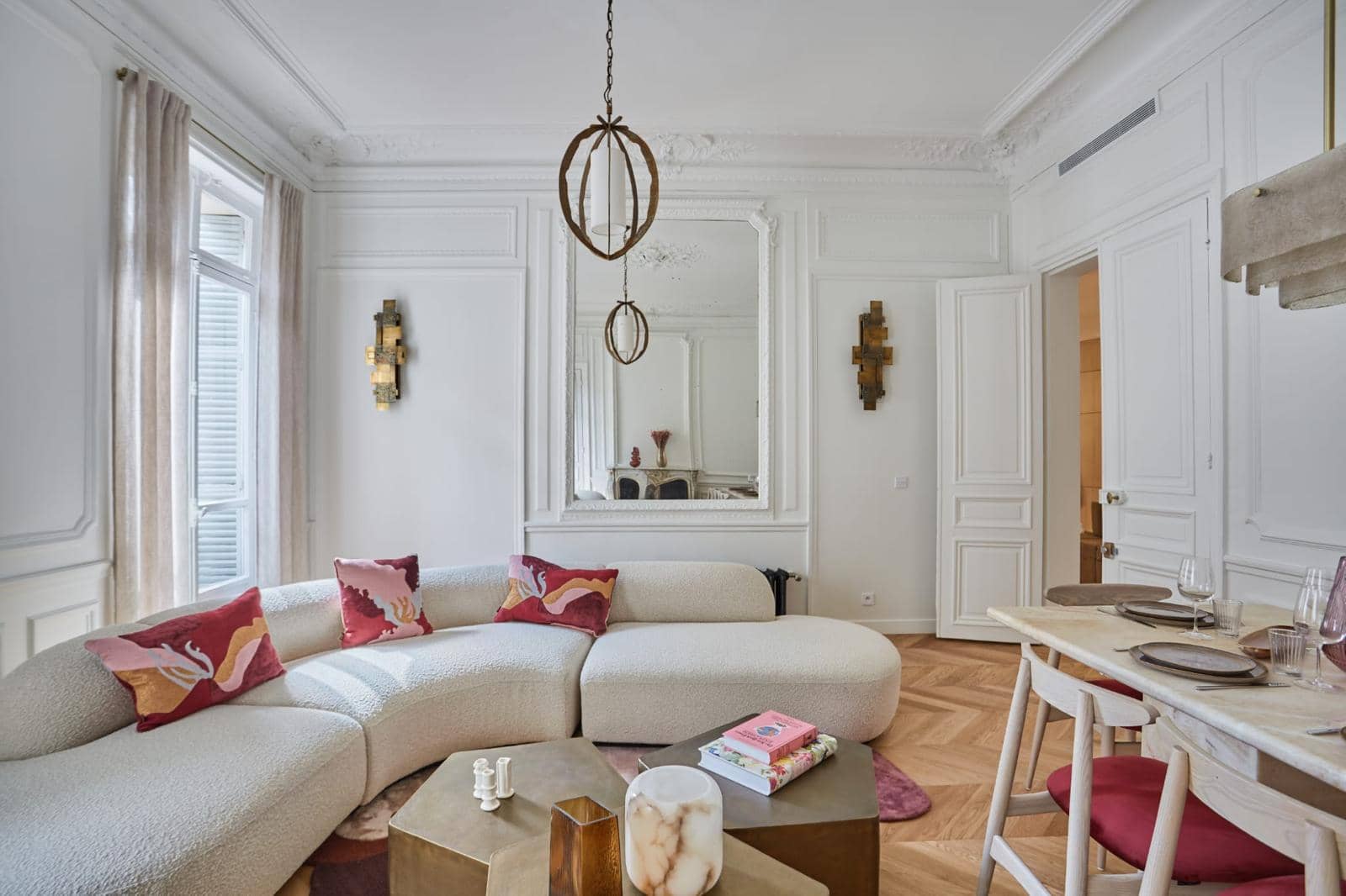 Salon ancien rénové : trumeau en miroir, moulures au plafond, appliques dorées, canapé courbe et parquet en chevrons