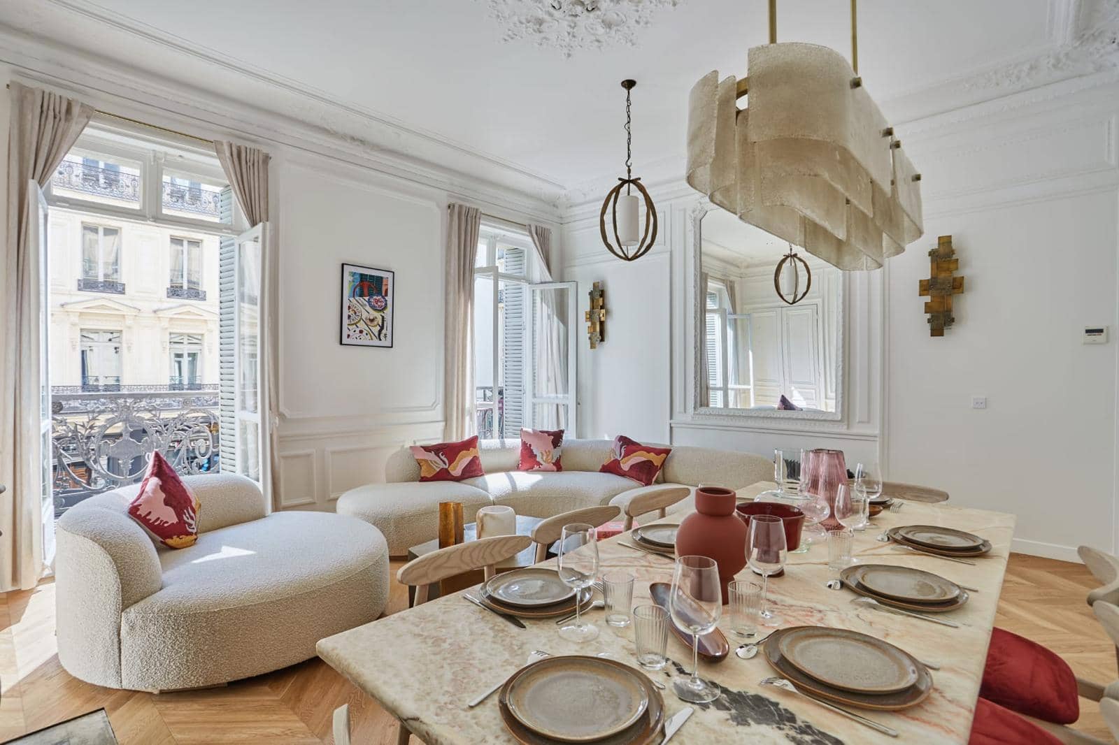 Séjour d'un appartement haussmannien rénové : table en marbre, canapé courbe, moulures et porte-fenêtre sur balcon