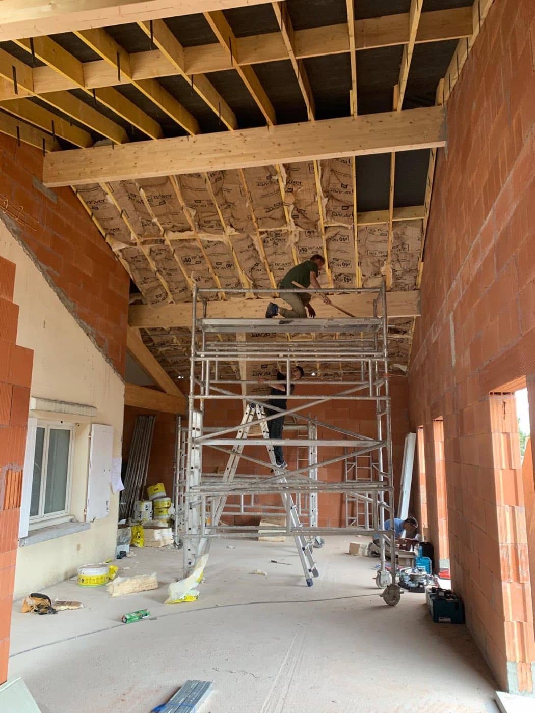 Surélévation en cours : murs neufs en brique, solivage bois isolé sous toiture et échafaudage intérieur